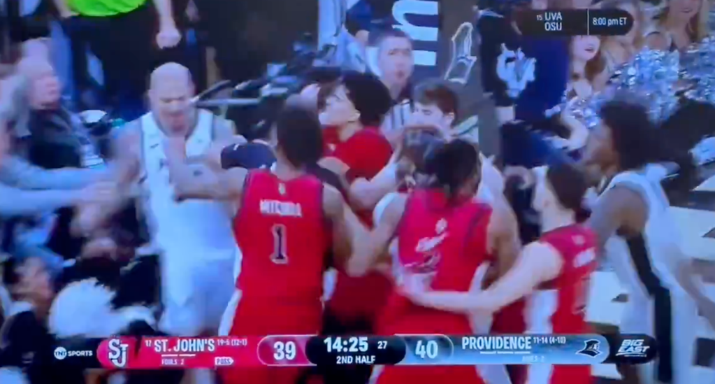 Basketball players from St. John's and Providence teams in a huddle on court during a game.